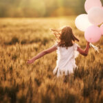 Girl running through field holding pink balloons