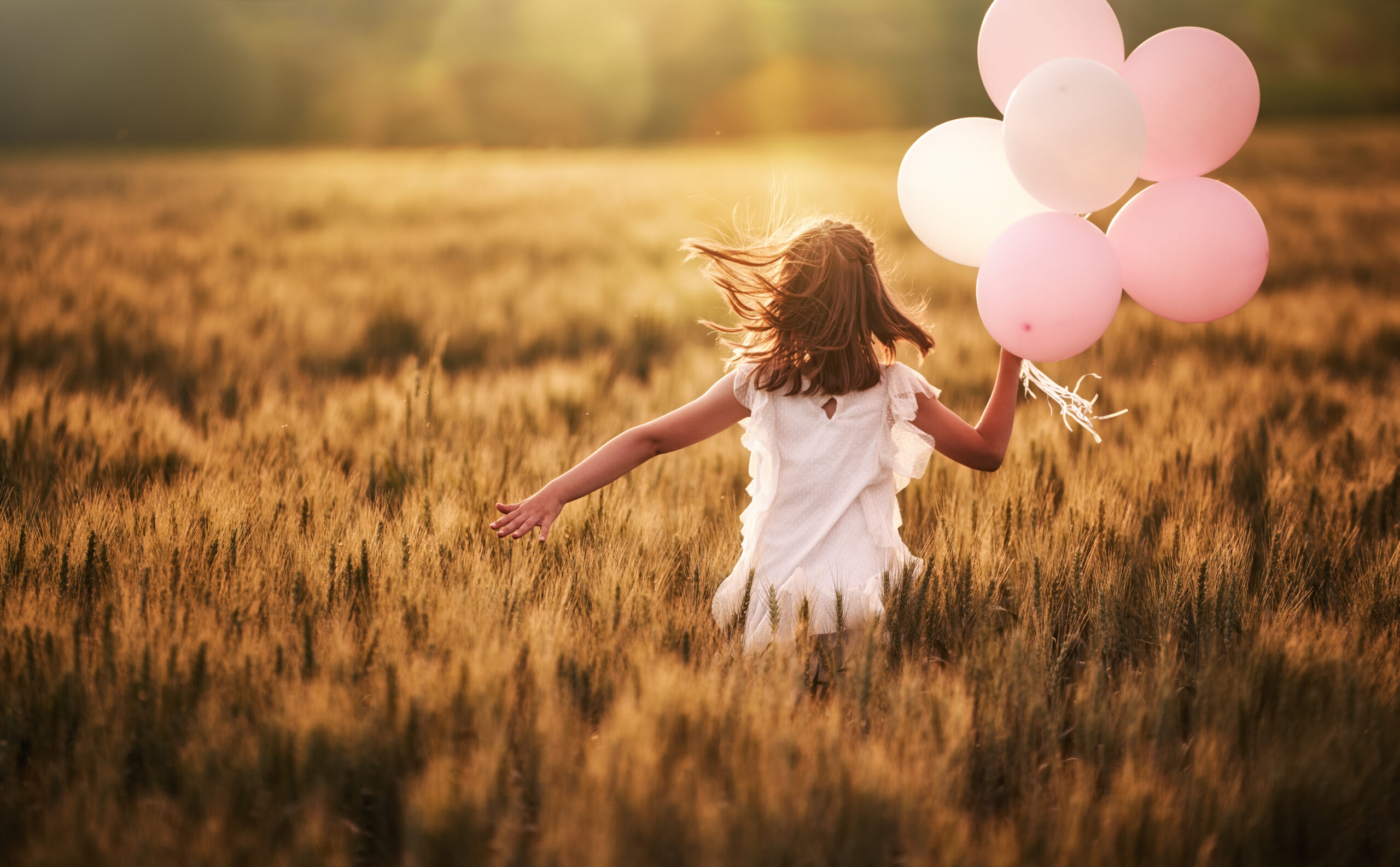 Girl running through field holding pink balloons