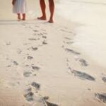 two people walking on the beach barefoot
